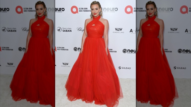 Hilary Duff con el pelo peinado hacia atrás posando en un evento con un vestido rojo brillante con falda amplia.