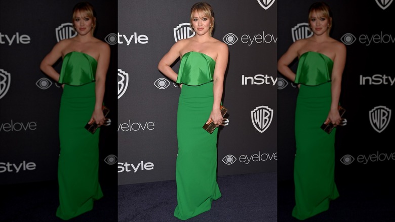 Hilary Duff posando en un evento con la mano en la cadera luciendo un vestido palabra de honor en color verde esmeralda.
