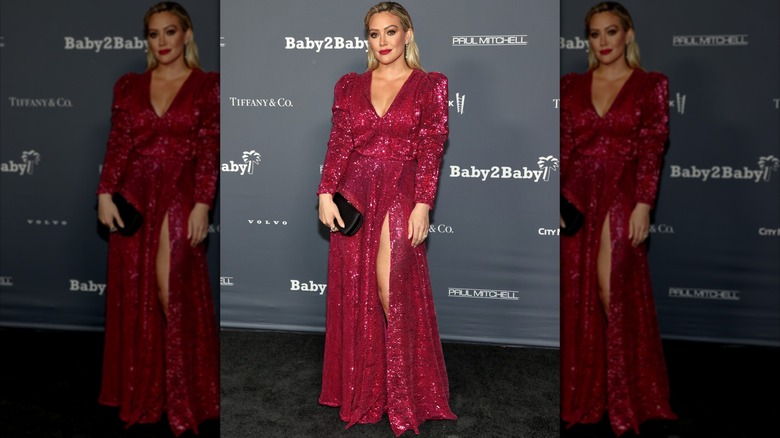 Hilary Duff en un evento de alfombra roja posando con un vestido rojo brillante con escote en V profundo y abertura en la falda.