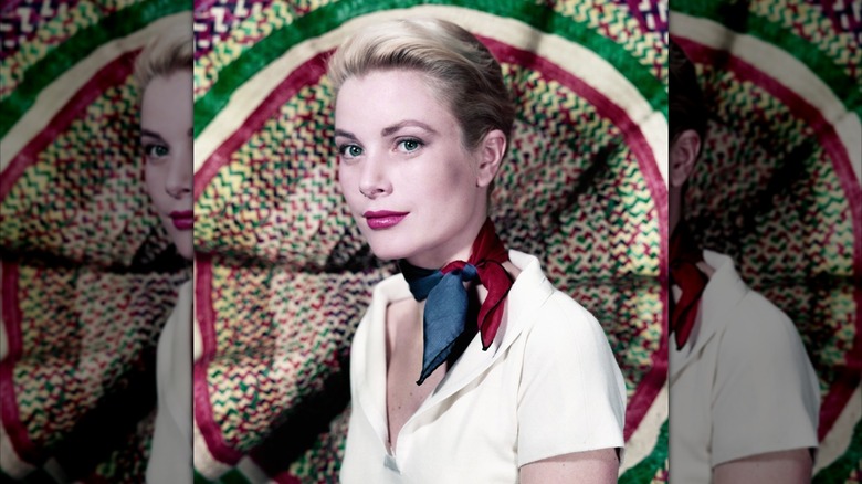 Grace Kelly con el pelo recogido y vistiendo una camisa blanca y un pañuelo azul y rojo delante de un fondo colorido.