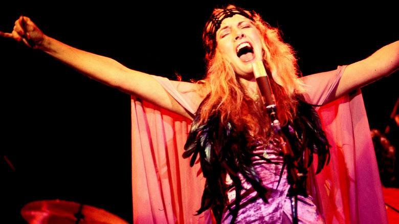 Stevie Nicks con los brazos extendidos cantando con una capa fluida y un traje de plumas actuando con Fleetwood Mac en 1978.
