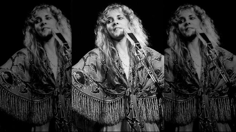 Fotografía en blanco y negro de Stevie Nicks frente a un micrófono con un top con flecos de cachemira actuando con Fleetwood Mac en 1978.