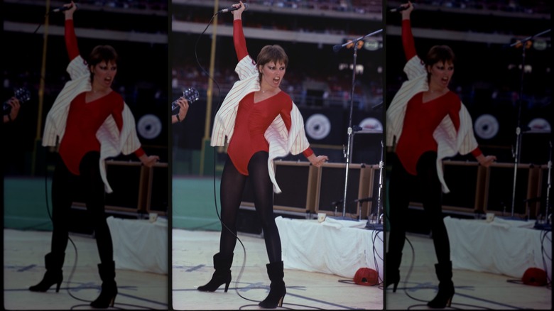 Pat Benatar vistiendo un mono rojo con calzas negras y botas actuando en el escenario.