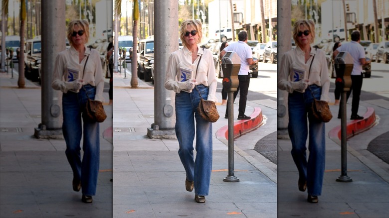 Melanie Griffith sostiene un libro con jeans anchos y una blusa blanca.