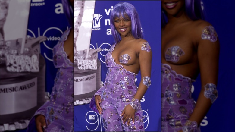 Lil Kim en los MTV VMA de 1999 con un mono color lavanda adornado y un pecho sobresaliendo cubierto por una empanada morada.