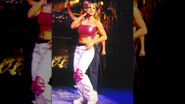 Britney Spears en el escenario con un top de tubo rosa intenso y pantalones cargo blancos.