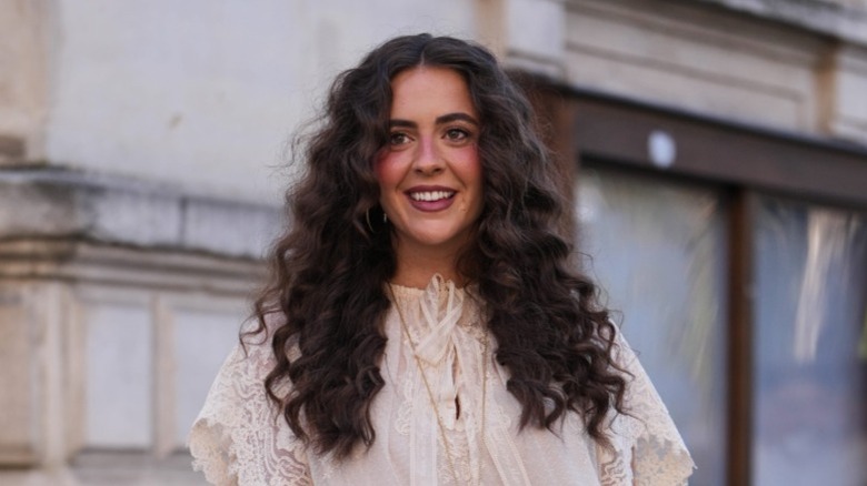 Una mujer con cabello largo y voluminoso y rizado sonríe.