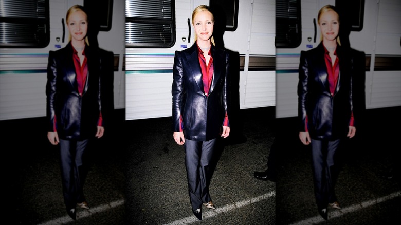Lisa Kudrow llevaba una chaqueta de cuero negra con una camisa roja y pantalones grises con el pelo peinado hacia atrás.