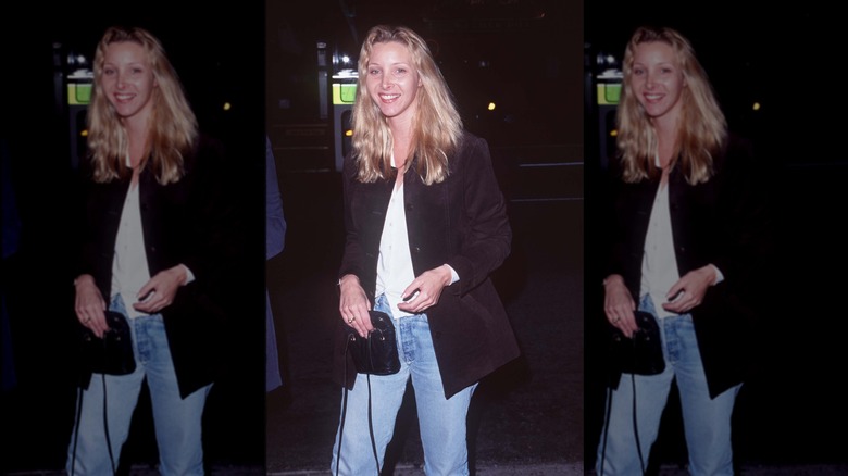 Lisa Kudrow vestida con jeans, camisa blanca y chaqueta negra, con cabello largo y ondulado.