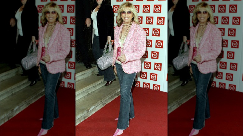 Nancy Sinatra posando en una alfombra roja luciendo jeans oscuros con una chaqueta rosa y zapatos rosas.