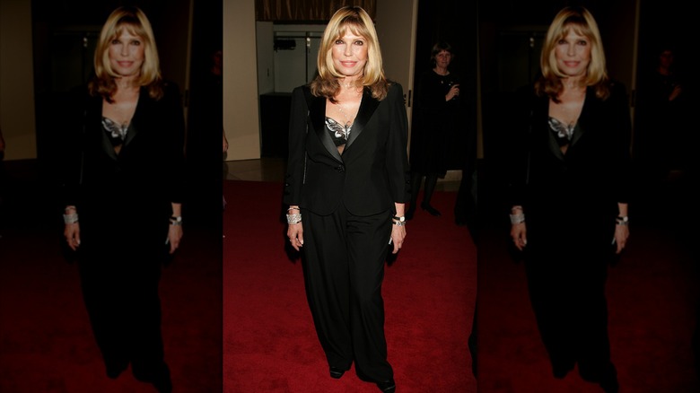 Nancy Sinatra en un evento de alfombra roja luciendo un traje completamente negro con el pelo suelto.