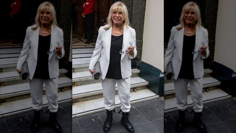 Nancy Sinatra fue fotografiada afuera sosteniendo sus gafas y vistiendo pantalones blancos, una chaqueta con una camisa negra y botas de combate.