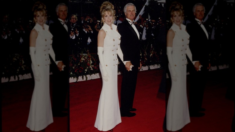 Jane Fonda posando en la alfombra roja de los Premios de la Academia luciendo un vestido blanco con botones dorados y guantes largos blancos.