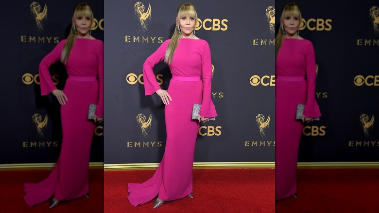 Jane Fonda posando en la alfombra roja con un vestido rosa brillante y el pelo recogido en una coleta baja con flequillo contundente.