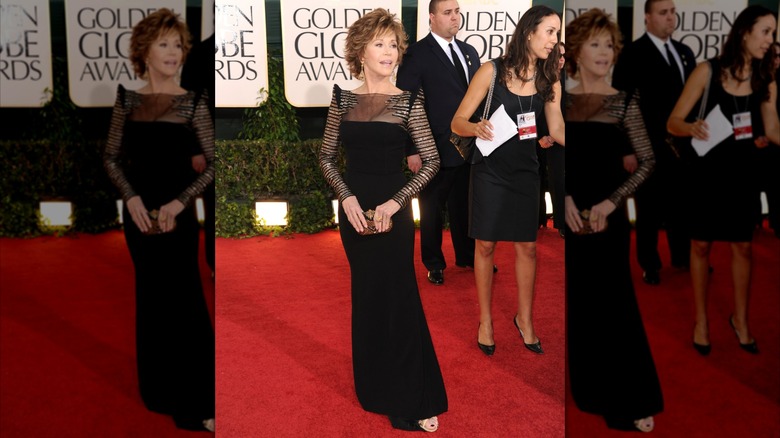 Jane Fonda posando en la alfombra roja de los Globos de Oro con un vestido largo negro con detalles en mangas y hombros.