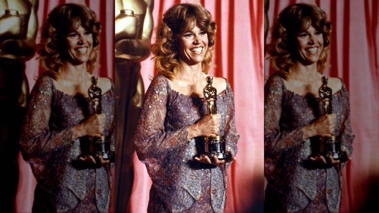 Jane Fonda posando con su Premio de la Academia con un vestido morado fluido y el cabello rizado.