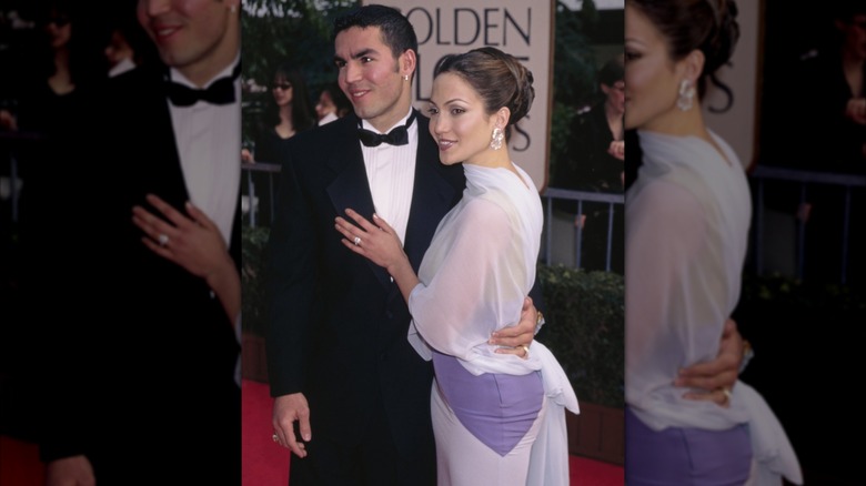 Jennifer López con vestido blanco y lila y moño alto junto a Ojani Noa con esmoquin negro.