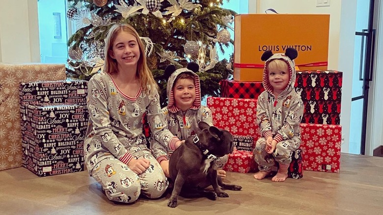 Los hermanos Taylor, Brayden y Hudson posan con su perro frente a un árbol de Navidad y regalos en pijamas navideños.