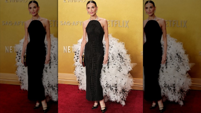 Demi Moore posando en la alfombra roja con un vestido negro sin mangas con una esponjosa cola blanca y negra.