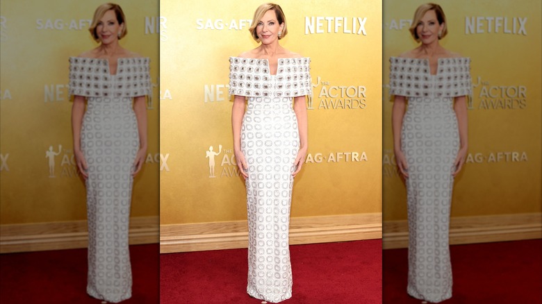 Allison Janney posando en la alfombra roja con un vestido blanco con estampado geométrico y hombros descubiertos.