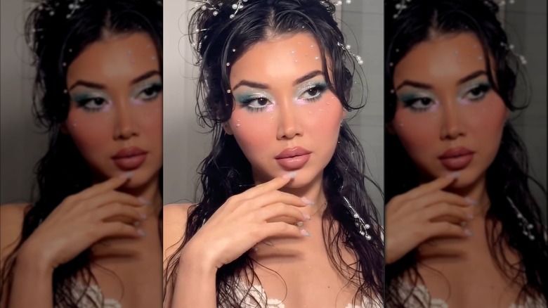 Una mujer con maquillaje estilo sirena, con sombra de ojos azul verdoso y rubor bañado por el sol.