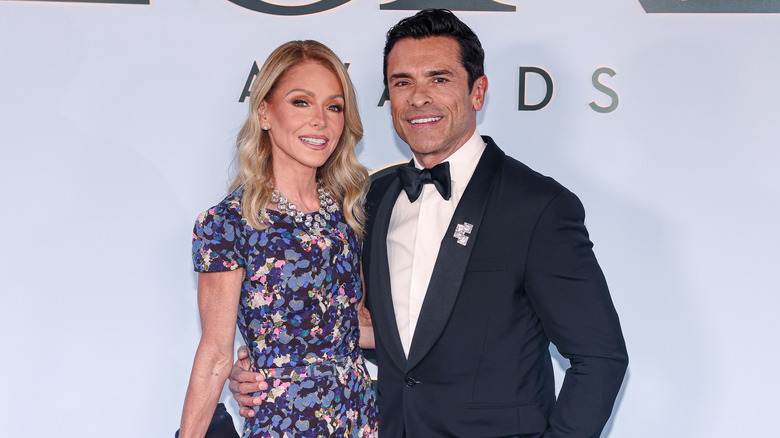 Kelly Ripa con un vestido floral morado junto a Mark Consuelos con un esmoquin azul marino.