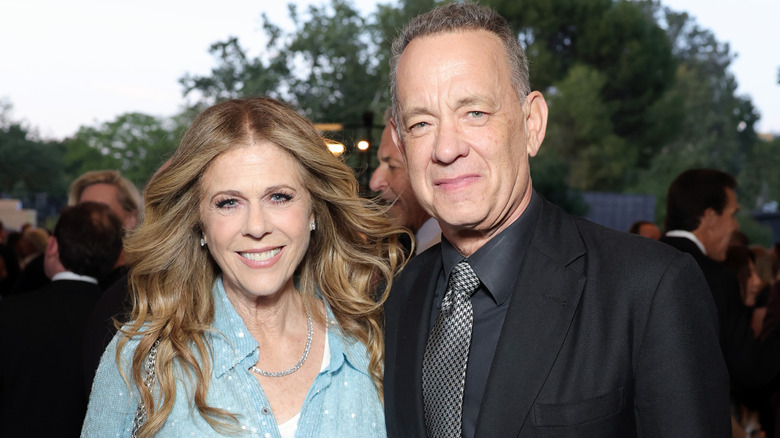 Rita Wilson con un top azul celeste y el pelo suelto junto a Tom Hanks con un traje negro.
