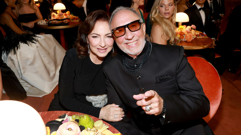 Gloria Estefan con un vestido negro, sentada junto a su esposo Emilio Estefan vestido completamente de negro.