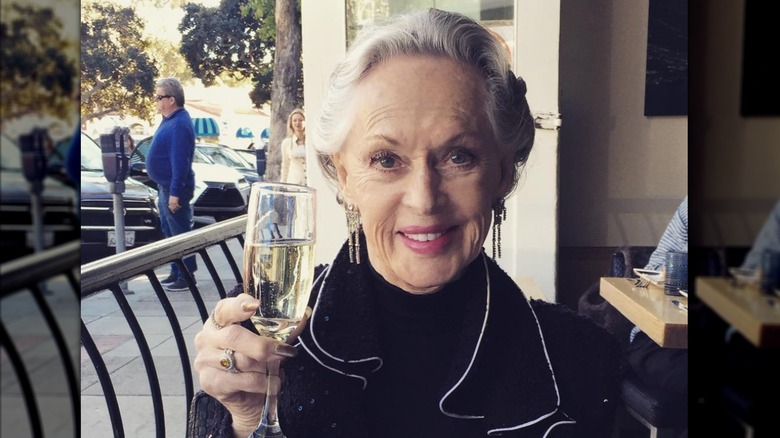Tippi Hedren viste una chaqueta negra y sostiene una copa de champán mientras cena en un restaurante.