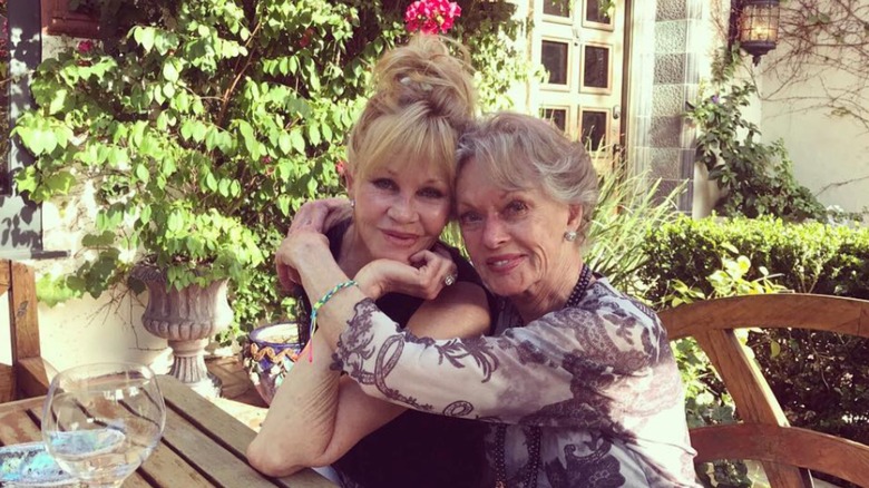 Melanie Griffith y Tippi Hedren se abrazan mientras posan para una foto al aire libre en una mesa de picnic.
