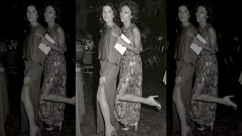 Rita Moreno con un vestido floral sin tirantes con la pierna echada hacia atrás y Linda Lavin con un vestido fluido en los premios Emmy de 1978.