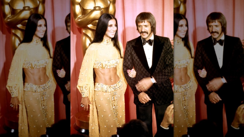 Cher con un traje de dos piezas dorado brillante posando del brazo de Sonny Bono con un esmoquin estampado marrón.