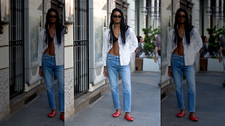 Una mujer con camisa blanca, jeans y bailarinas rojas.