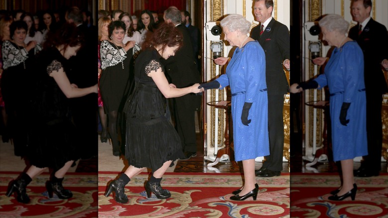 Helena Bonham Carter haciendo una reverencia con un vestido negro y botas estrechando la mano de la reina Isabel. usando un vestido azul.