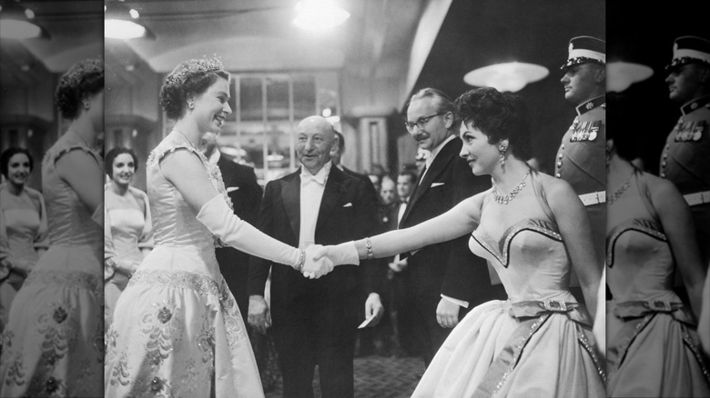Gina Lollobrigida con un vestido escotado y estrechándole la mano a la reina Isabel.