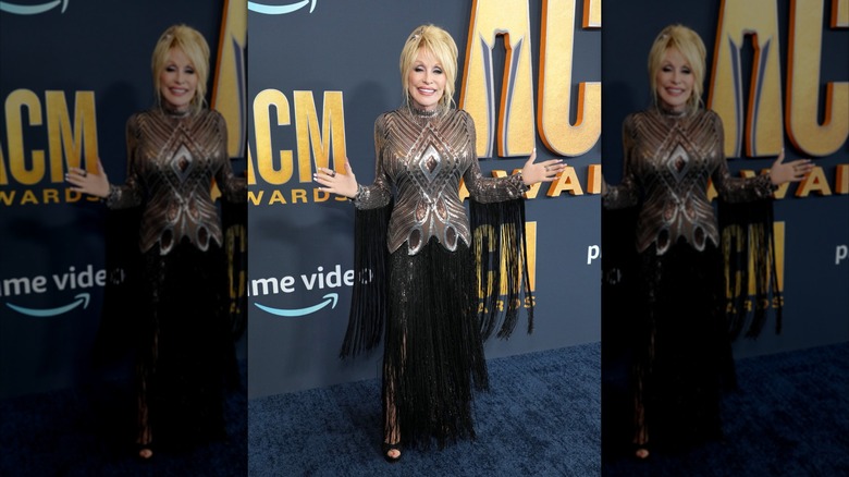 Dolly Parton con los brazos abiertos luciendo un vestido metalizado con flecos negros en los Premios ACM 2022.