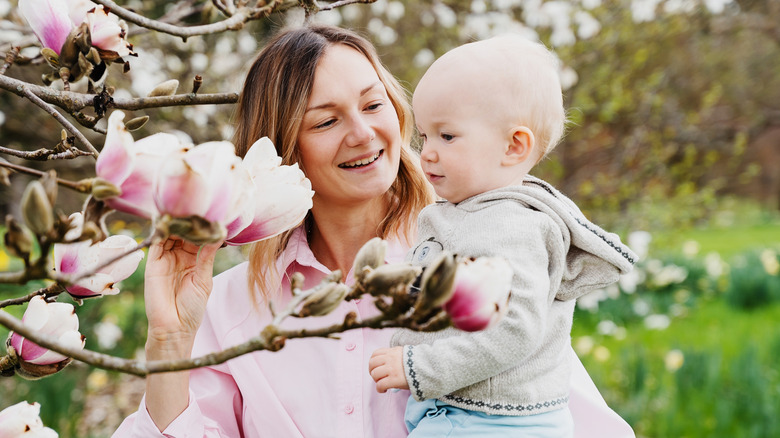 Madre sosteniendo a su bebé junto a un árbol en flor
