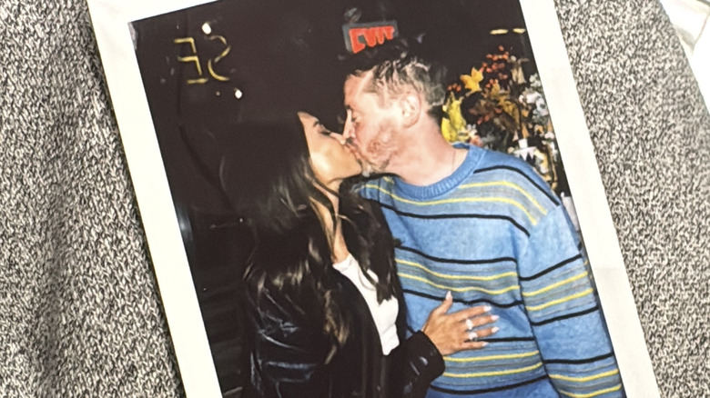 Una foto de una Polaroid con Brenda Song con una chaqueta de cuero besando a Macaulay Culkin con un suéter a rayas.