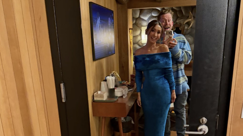 Brenda Song lleva un vestido de gamuza azul mientras Macaulay Culkin está detrás de ella con un cómodo suéter y jeans.