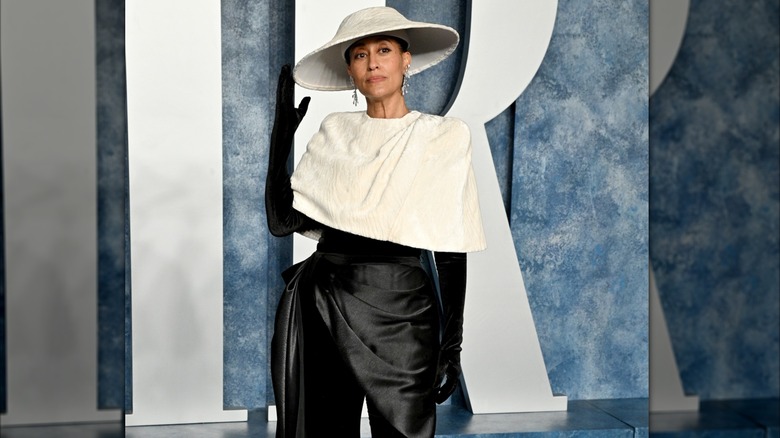 Tracee Ellis Ross posando en un evento de alfombra roja luciendo un conjunto negro y guantes con una gorra blanca y un sombrero blanco.