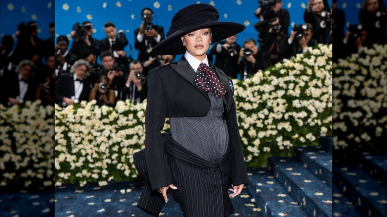 Rihanna posando en la Met Gala 2025 con un atuendo inspirado en la ropa masculina con una pajarita flexible y un gran sombrero negro.