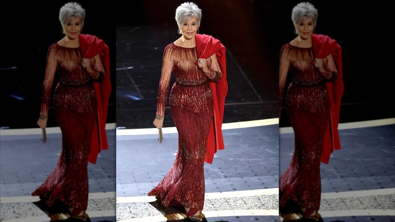 Jane Fonda posando en los Premios de la Academia con un vestido rojo brillante y un abrigo rojo brillante sobre el hombro.