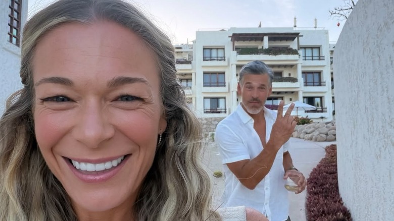 LeAnn Rimes sonríe en el frente mientras Eddie Cibrian hace el signo de la paz en el fondo.