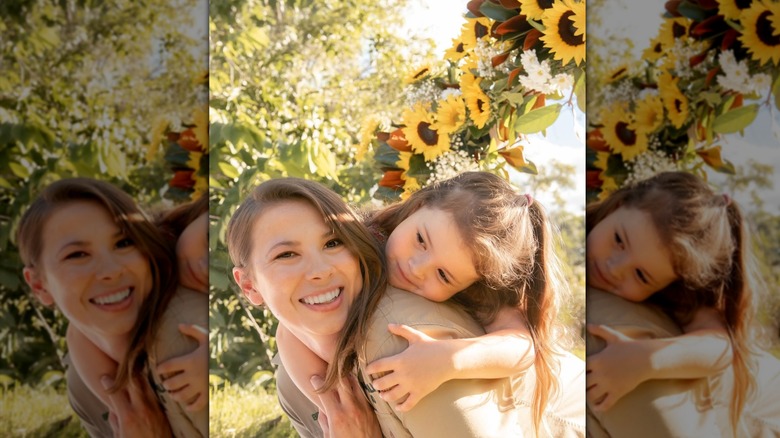 Bindi Irwin abrazando a su hija Grace debajo de una guirnalda de girasoles