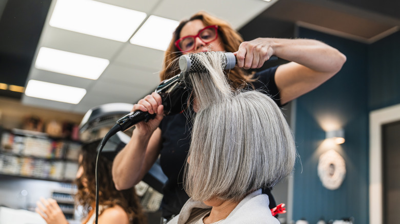 Mujer con un bob gris en un salón con su cabello peinado con secador y cepillo.
