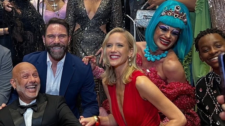 Jessy Schram posa con un grupo de personas con labios rojos y un vestido rojo recortado
