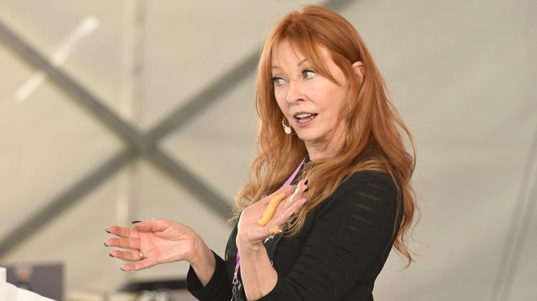 Cassandra Peterson dando una charla vestida con un top negro y su largo y ondulado cabello rojo suelto.