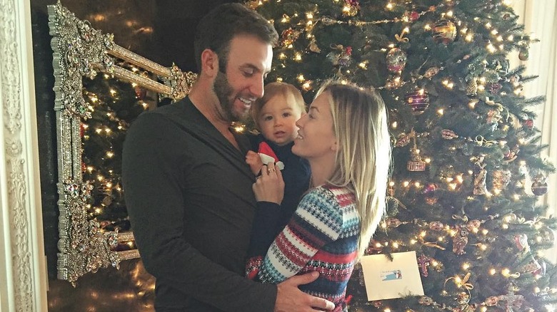 Dustin Johnson y Paulina Gretzky abrazan a su bebé, Tatum Johnson, frente a un árbol de Navidad.