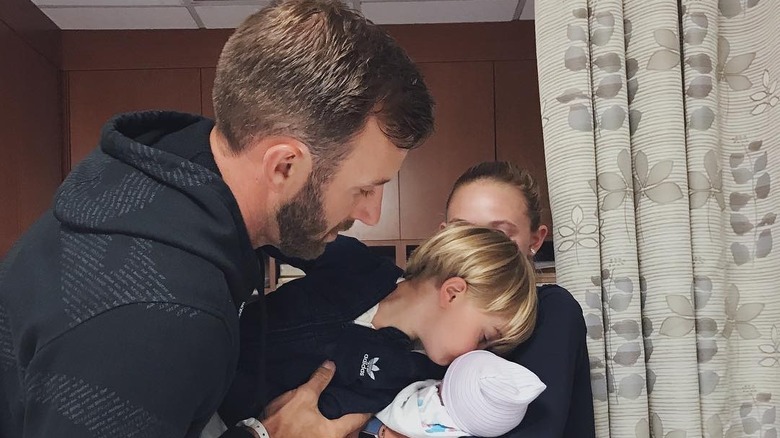 Dustin Johnson sostiene a Tatum Johnson mientras besa a su hermano recién nacido, River Johnson, quien parece estar sostenido por Paulina Gretzky.