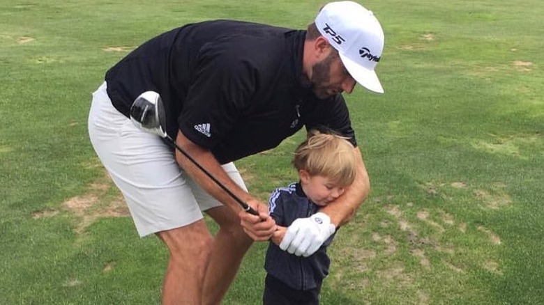 Dustin Johnson ayuda a su hijo, Tatum Johnson, a hacer swing con un palo de golf.